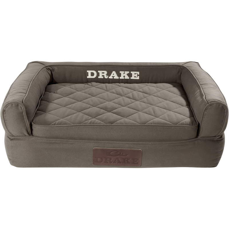 Team Gun Dog Landing Zone Premium Canvas Dog Couch, a bolster-style pet bed with raised sides, quilted cushion, memory foam, and DRAKE stitched on the back.