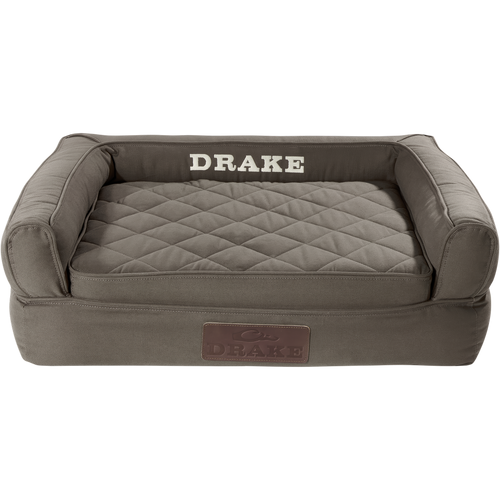 Team Gun Dog Landing Zone Premium Canvas Dog Couch, a bolster-style pet bed with raised sides, quilted cushion, memory foam, and DRAKE stitched on the back.