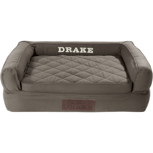 Team Gun Dog Landing Zone Premium Canvas Dog Couch, a bolster-style pet bed with raised sides, quilted cushion, memory foam, and DRAKE stitched on the back.