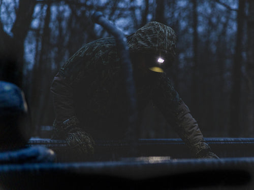 Lumen Camo Headlamp EVO1000 on a person in a dark room, featuring a camouflage-patterned headband and flashlight, ideal for hunting with hands-free lighting.