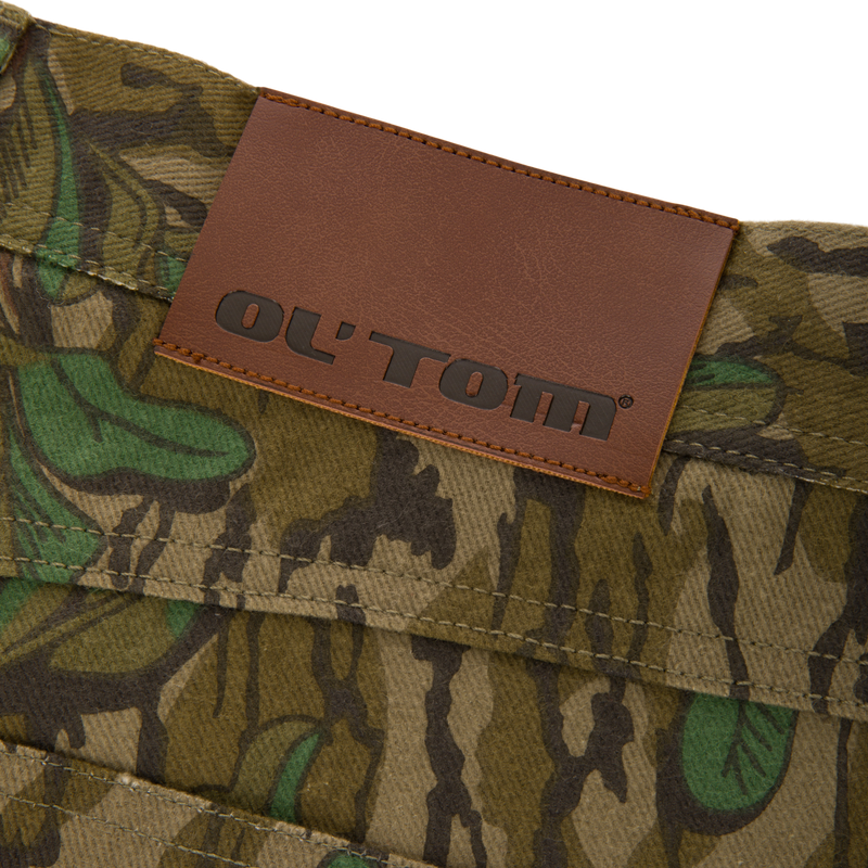 Throwback 80 Field Pant close-up featuring a brown leather label on durable camouflage cotton twill, highlighting reinforced stitching and antique brass details for rugged functionality.