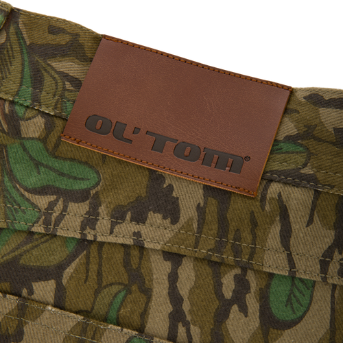 Throwback 80 Field Pant close-up featuring a brown leather label on durable camouflage cotton twill, highlighting reinforced stitching and antique brass details for rugged functionality.