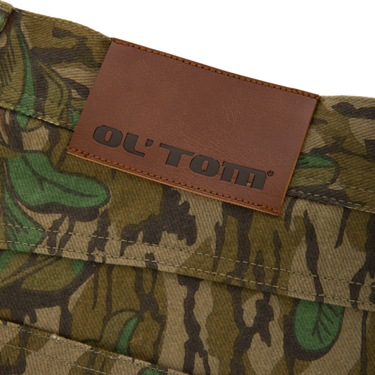 Throwback 80 Field Pant close-up featuring a brown leather label on durable camouflage cotton twill, highlighting reinforced stitching and antique brass details for rugged functionality.