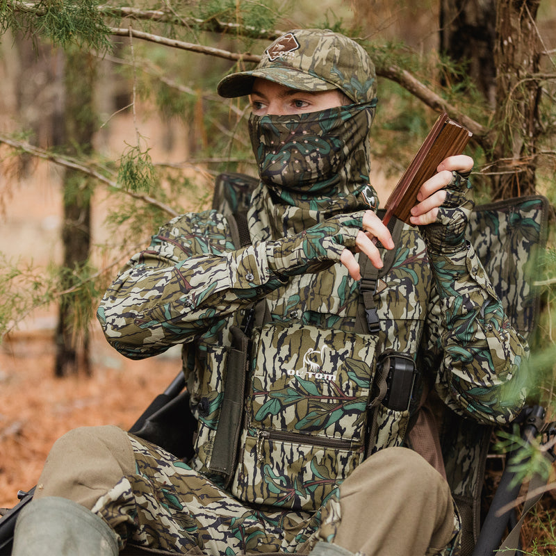 Turkey Chest Pack with removable bino harness, multiple pockets, and loops, designed for efficient hunting gear organization, showcased by a man in camouflage holding gear.