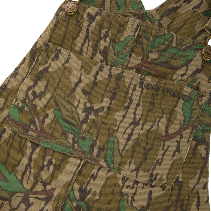 Throwback 80 Field Bib, camouflage overall, showcasing durable cotton twill, antique brass details, and reinforced knees, ideal for hunting and rugged tasks.