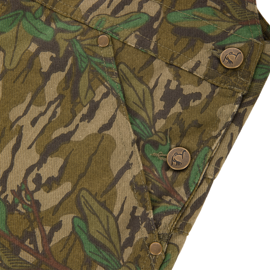 Close-up of the Throwback 80 Field Bib showing camouflage fabric, antique brass buttons, and riveted pockets, emphasizing durability and vintage style for rugged tasks.