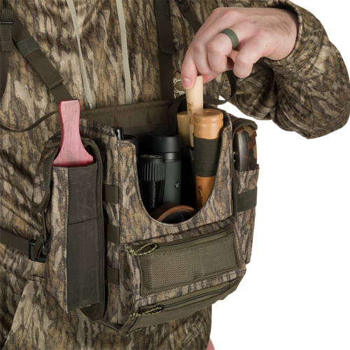 Turkey Chest Pack, lightweight and durable, held by person in camouflage. Features multiple pockets, removable bino harness, and stowable rain fly for hunting convenience.
