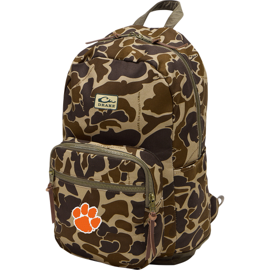 Clemson Throwback 80 Backpack with camo pattern, two front zippered compartments, side pockets, leather pulls, and an orange paw-print logo on durable canvas.