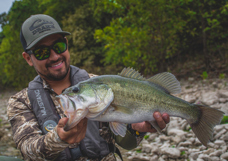 A man holding a fish while wearing the DPF Stretch Fit Cap, a comfortable and stylish accessory for summer fishing.