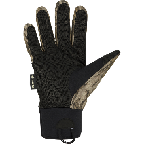 A black glove with a camouflage pattern, perfect for early season waterfowl hunting. Made with waterproof Refuge HS™ shell fabric and GORE-TEX® membrane for 100% waterproof/breathable protection. Features include a digitized goat skin leather palm and gusseted neoprene cuffs. Stay-Put™ liner system ensures no twisting or bunching. Adjustable gusset Velcro cuff closure and pull loop assist for easy use. From Purewhitelaneshop, your go-to store for high-quality hunting gear and clothing.