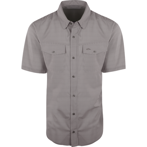 A close-up of the Traveler's Check Shirt S/S, a lightweight and breathable shirt with four-way stretch for freedom of movement. Features moisture-wicking fabric and two chest pockets with button flaps. Ideal for the man on the go.