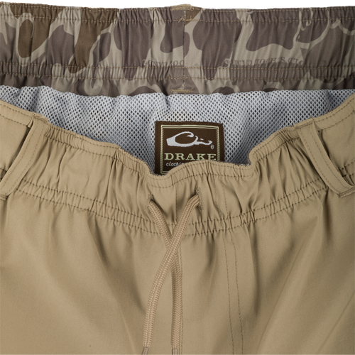 A pair of khaki Dock Swim Trunk Shorts with a label, zipper, and fabric close-ups. Made of durable nylon/spandex blend with water-resistant finish. Features elastic waist, mesh pockets, and 6
