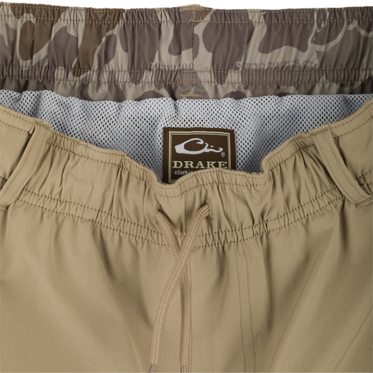A pair of khaki Dock Swim Trunk Shorts with a label, zipper, and fabric close-ups. Made of durable nylon/spandex blend with water-resistant finish. Features elastic waist, mesh pockets, and 6" inseam. Perfect for outdoor activities.