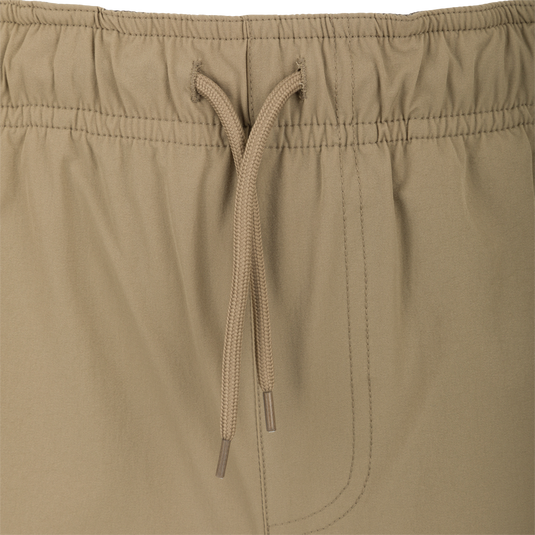 Dock Short 6" - A close-up of khaki swim trunks made from durable 90% Nylon and 10% Spandex fabric. Features include a water-resistant DWR finish, elastic waist with drawstring, and multiple mesh-lined pockets, including a bonus pliers pocket. Perfect for transitioning from boat to dock.