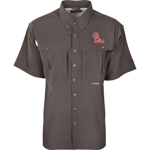 A close-up of the Ole Miss S/S Flyweight Wingshooter shirt, featuring a logo on a grey background. Made with ultra-lightweight polyester, it offers quick-drying, moisture-wicking, and breathable properties. Includes Sol-Shield™ UPF 50+ sun protection, Magnattach™ vertical chest pocket, and a vertical zipper pocket. Ideal for warm-weather outdoor activities.