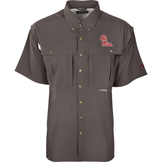 A close-up of the Ole Miss S/S Flyweight Wingshooter shirt, featuring a logo on a grey background. Made with ultra-lightweight polyester, it offers quick-drying, moisture-wicking, and breathable properties. Includes Sol-Shield™ UPF 50+ sun protection, Magnattach™ vertical chest pocket, and a vertical zipper pocket. Ideal for warm-weather outdoor activities.